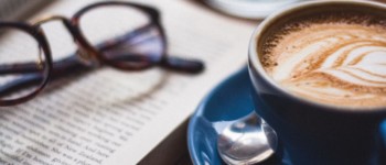 lunettes posées sur un livre et une tasse de café sur une table