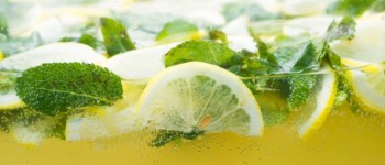 zoom sur la surface d'un verre de kéfir avec du citron et de la menthe, et en dessous la boisson de kéfir jaune et pétillante