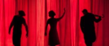 photo de silhouettes sur une scène derrière un rideau rouge dans un théâtre, deux dansent et une joue du violon