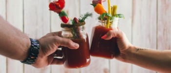 Deux bras qui trinquent avec des verres à cocktails contenant une boisson fruitée avec des pics garnis de fruits